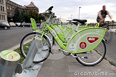 Bicycles on a public bike-sharing systems docking station. A man is cycling on the background. Editorial Stock Photo