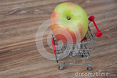 Big apple laying in shopping cart. Wooden background Stock Photo