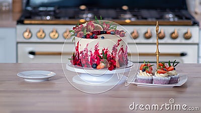 Big beautiful red velvet cake, with flowers and berries on top. Delicious sweet muffins with cream, Stock Photo