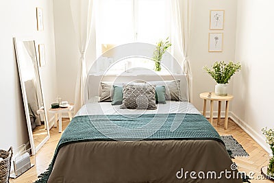 A big bed dressed in earth colors linen with cushions and a blanket standing in an eco friendly bedroom interior. Real photo. Stock Photo