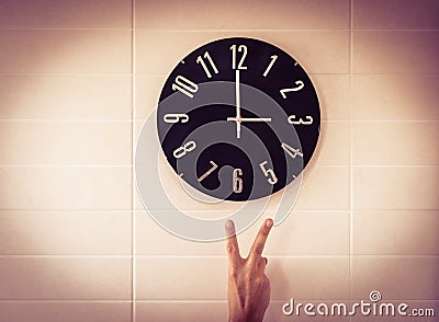 Big black clock on white wall. Time change. DST. Survey of the European Union on time change. Gesture of victory. Caucasian man. Stock Photo