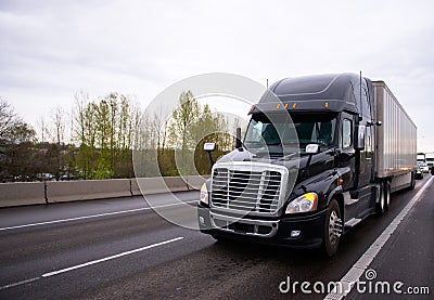 Big black modern semi truck rig trailer in traffic on highway Stock Photo