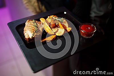 Big black plate with fried potatoes, meat and tomato sauce. Stock Photo