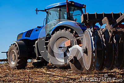 Big blue tractor plows the field and removes the remains of previously mown sunflower. Stock Photo