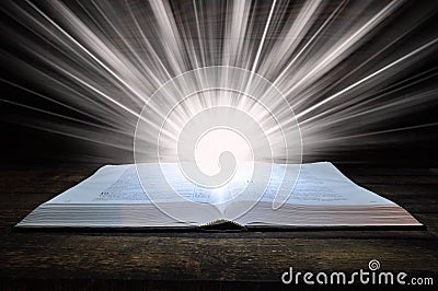 The big book of the Bible lies on a wooden table. In the dark. A light shines on the book from above. Light comes out of the book Stock Photo
