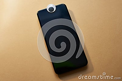 Big brother is watching you. Studio shot of an eye covering the webcam on a smartphone against a brown background. Stock Photo