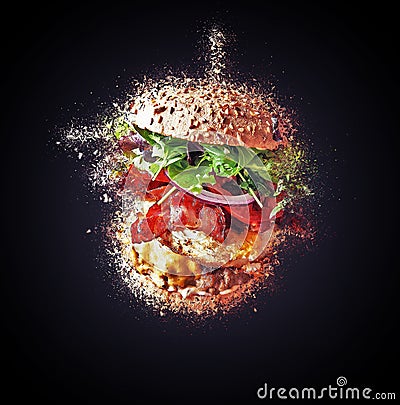 Big burger flying and exploding against Black Stock Photo