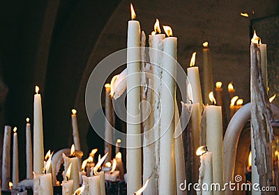 Big burning candles from prayers for hope. Saint Bernadette grotto with many white candles with flame. Sanctuary in Lourdes. Stock Photo