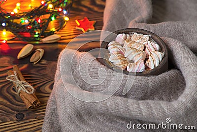 Big cup of hot cocoa with marshmallow, cinnamon and nurs and warm blanket on an old vintage wooden and Christmas light. Stock Photo