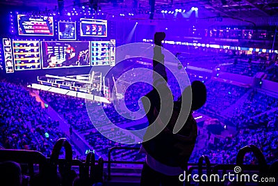 Big esports event. Video games fan on a tribune at tournament`s arena with hands raised. Cheering for his favorite team. Stock Photo