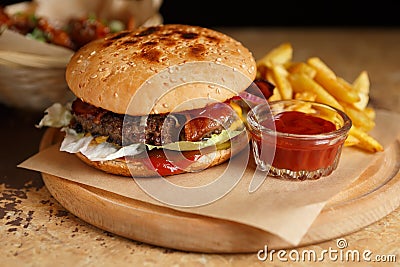 Big fat hamburger cooked on grill and served on wooden plate with fries and ketchup. Traditional American burger for dinner Stock Photo