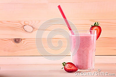 A big glass full of appetizing smoothie. A berry shake on a wooden background. Tasty milkshake with a straw and cut strawberries. Stock Photo