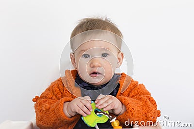 Medium horizontal shot of adorable fair toddler girl sitting in high chair holding colourful toy Stock Photo