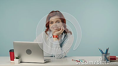 Medium isolated shot of a satisfied, happy and relaxed young woman sitting at the desk with laptop and working supplies Stock Photo