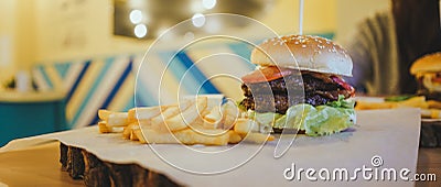A big juicy burger with two cutlets, vegetables, sauce and french fries on the table in a cafe. Stock Photo