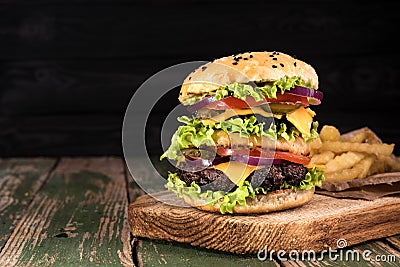 Big juicy hamburger with fried potato vegetables and beef on black wooden rustick background. Vintage toned Stock Photo