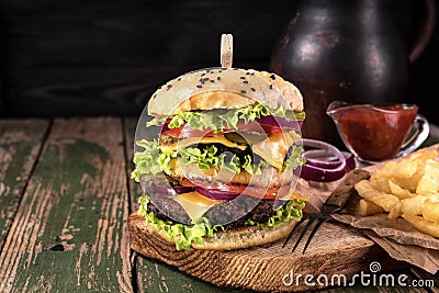 Big juicy hamburger with fried potato vegetables and beef on black wooden rustick background. Vintage toned Stock Photo