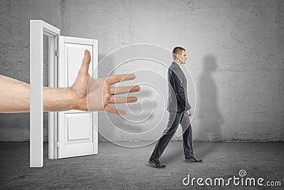 Big male open hand reaching through white doorway to young businessman who is walking away on grey wall background Stock Photo