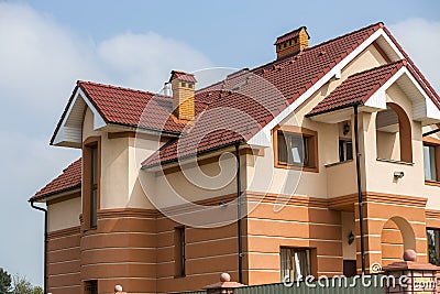 Big modern expensive luxurious residential two-stories cottage, family house with shingled brown roof, high brick chimneys, stucco Stock Photo