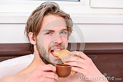 Big naked muscular man having fun in bedroom. Pleasant beginning of day. Handsome young man drink coffee and eating Stock Photo