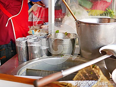 Big noodle broth pot, buckets, ladle, ingredient containers, and stanless cooking counter at a busy small noodles restaurant in Stock Photo