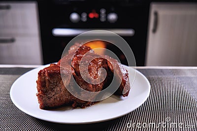 Big piece of meat on plate. Roast beef close-up. Barbecue meat in modern kitchen. Blurred background oven. Hot cooked dinner. Stock Photo