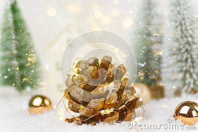 Big pine cone with golden garland lights in winter scene in forest with fir trees falling snow. Christmas New Years holiday magic Stock Photo