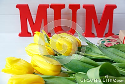 Big red letters Mum lies on the table with gift card and yellow tulips. Flowers for gift. Mother`s day concept. Stock Photo