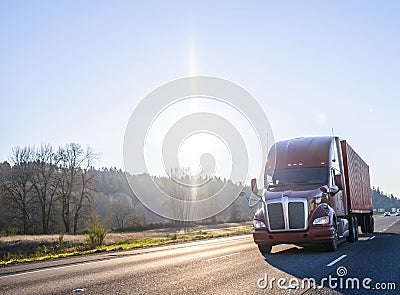 Big rig brown semi truck transporting container moving on the highway at sunshine day Stock Photo