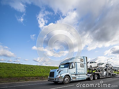 Big rig car hauler semi truck transporting cars on the special semi trailer driving on the flat road with green hill Stock Photo