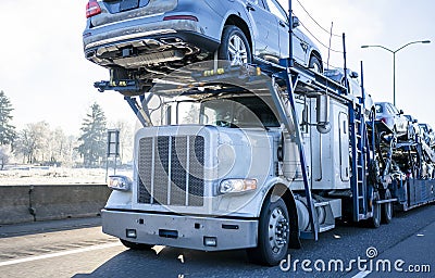 Big rig car hauler semi truck transporting cars on two levels semi trailer driving on winter frosty road Stock Photo