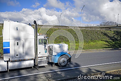 Big rig classic industrial transportation semi truck with chrome exhaust pipes and high cab running on the local road with hill on Stock Photo