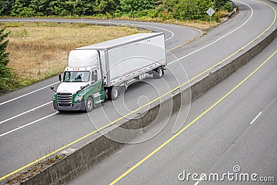 Big rig day cab semi truck with roof spoiler transporting dry van semi trailer running on the turning divided highway road with Stock Photo