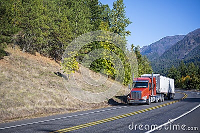 Big rig orange semi truck carry bulk semi trailer driving on win Stock Photo