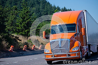 Big rig orange semi truck and trailer running on green highway w Stock Photo