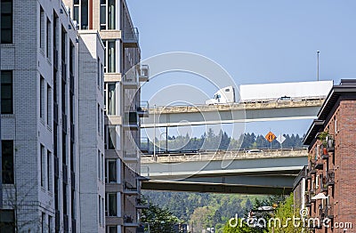 Big rig semi truck with semi trailer running on the overpass highway between high-rise buildings Stock Photo