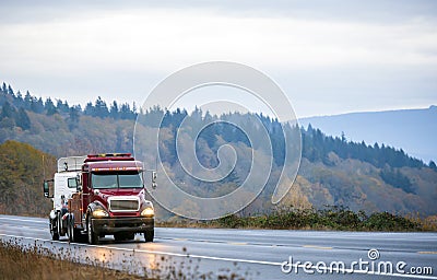 Big rig towing semi truck tow another semi truck on wet winding twilight autumn road in rain Stock Photo