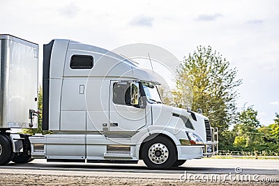 Big rig bonnet white long haul semi truck transporting cargo in dry van semi trailer driving on the highway road for timely Stock Photo