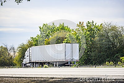 Big rig white long hauler semi truck with high cab transporting commercial cargo in dry van semi trailer running on the road with Stock Photo