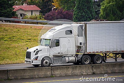 Big rig white semi truck transporting commercial cargo in refrigerator semi trailer running on the autumn divided highway Stock Photo