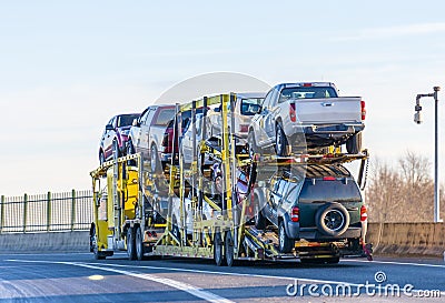 Big rig yellow car hauler semi truck transporting cars on two levels semi trailer driving on the overpass road Stock Photo