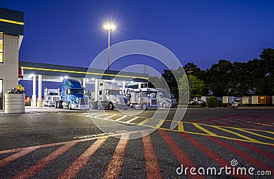 Big rigs semi trucks standing on the truck stop parking lot under a lighted awning at night Stock Photo