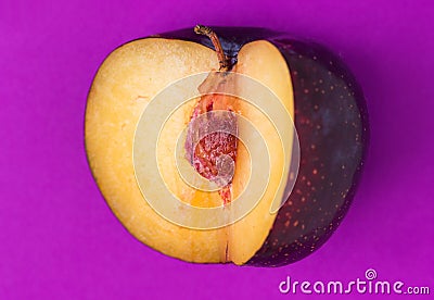 Big ripe organic purple plum with cut out segment on ultra violet background. Yellow flesh pit close up. Creative minimalist Stock Photo