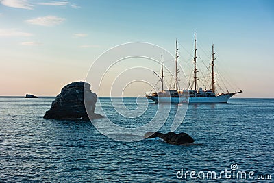 Big rock and sailing ship at sunset in front of city harbor, Skopelos island Stock Photo