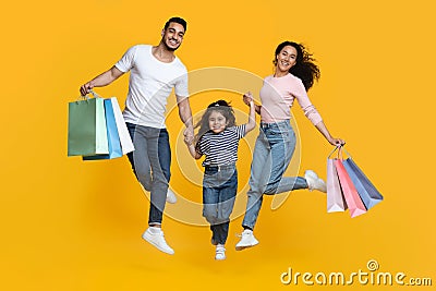 Big Shopping Concept. Overjoyed Arab Family Of Three Jumping With Shopper Bags Stock Photo