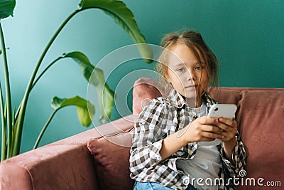 Medium shot portrait of pretty adorable little child girl using smartphone looking at camera, watching cartoons, Stock Photo