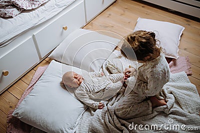 Big sister playing with newborn, little baby. Girl looking at new sibling, holding baby& x27;s small feet. Sisterly love Stock Photo