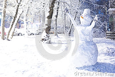 Big snowman in the yard after a snowfall in winter. Nose-carrot, bucket on the head, gloves on the hands, eyes. Cars in the snow Stock Photo