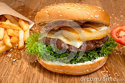 Big tasty burger on the wooden table with becon and french fries. Delicious dinner with cheese, tomatoos and salad. Fast food with Stock Photo