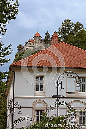 Big two-storied residential building with red tile roof. Famous Bled Castle at the cliff in the background. Stock Photo